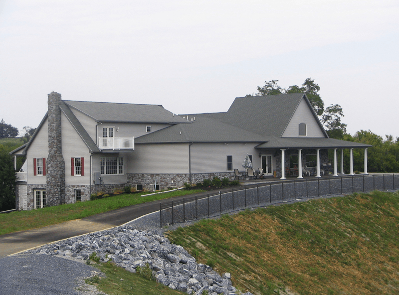 Large gray house with stone chimney, porch with white columns, and black fence.