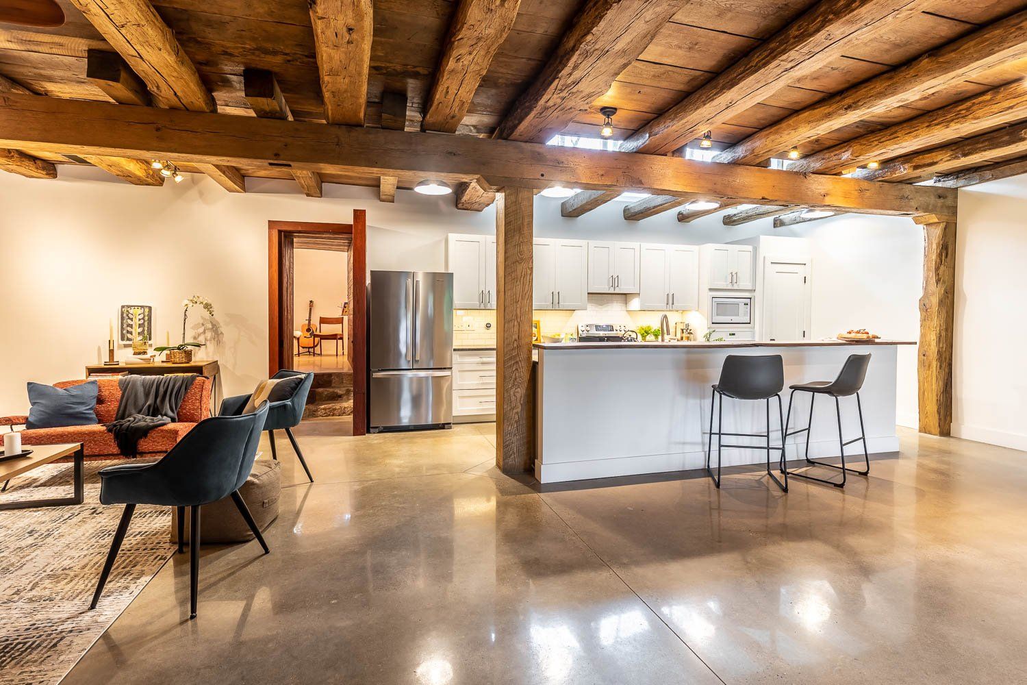 Open-concept living space with exposed wooden beams, polished concrete floor, and modern kitchen.