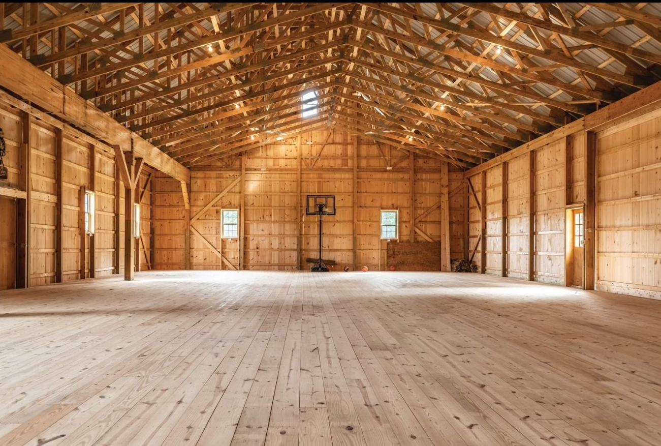 Interior of a large wooden barn with basketball hoop; natural light streams through windows.