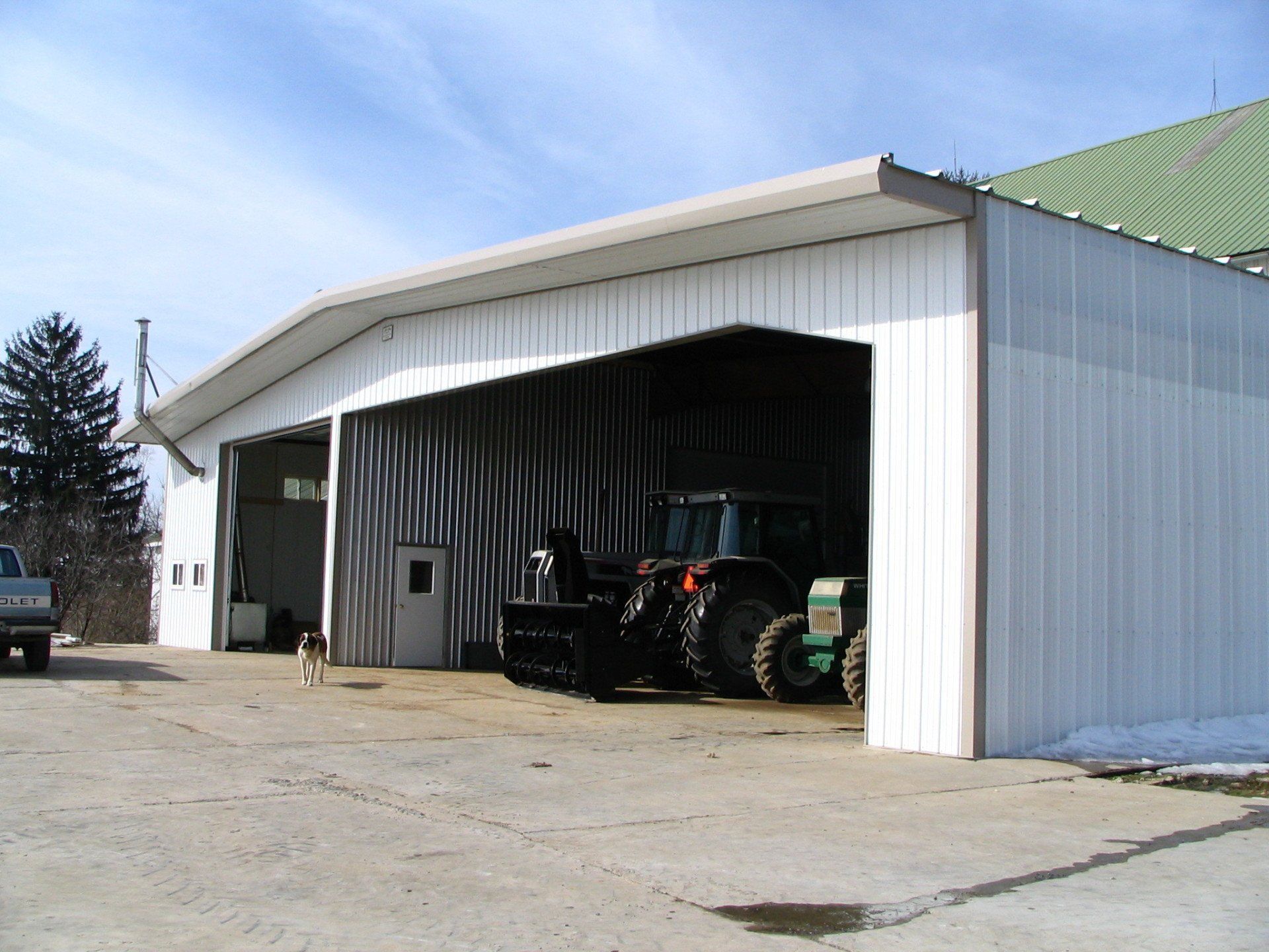 White farm building with open bay housing a green tractor.