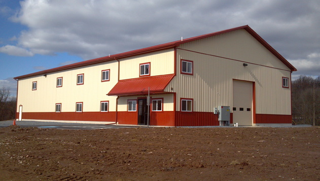 Large beige and red metal building with a red roof and loading door.