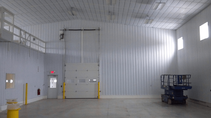 Empty industrial warehouse interior, white walls, large bay door, scissor lift.