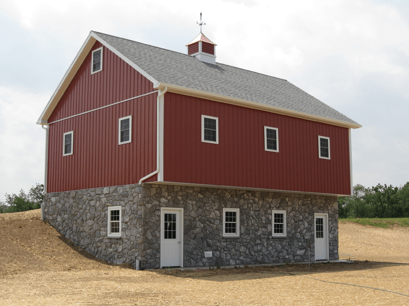 Red barn with gray roof, white trim, and stone foundation.