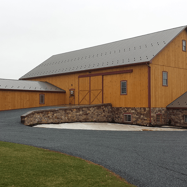 Wooden barn with a brown metal roof and stone foundation; asphalt driveway.