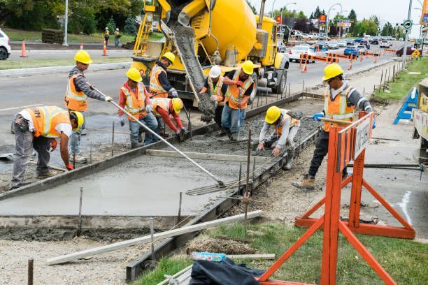 Construction workers pouring concrete for a sidewalk alongside a street, using tools and machinery.