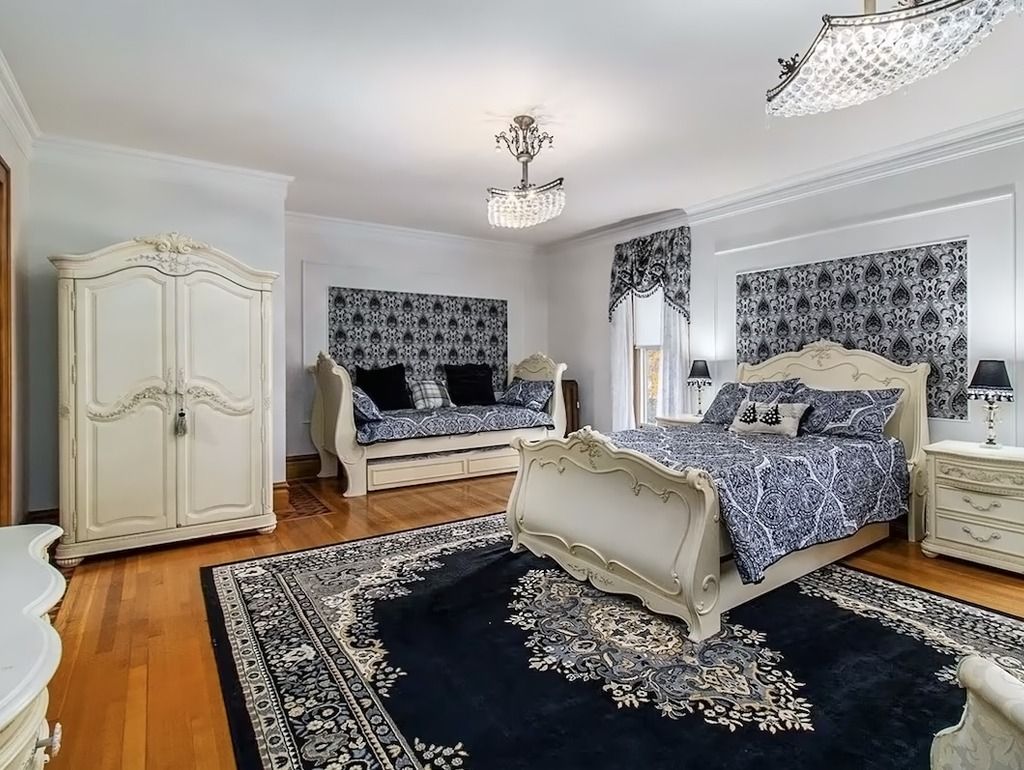 Ornate bedroom with white furniture, dark blue rug, and patterned bedding.