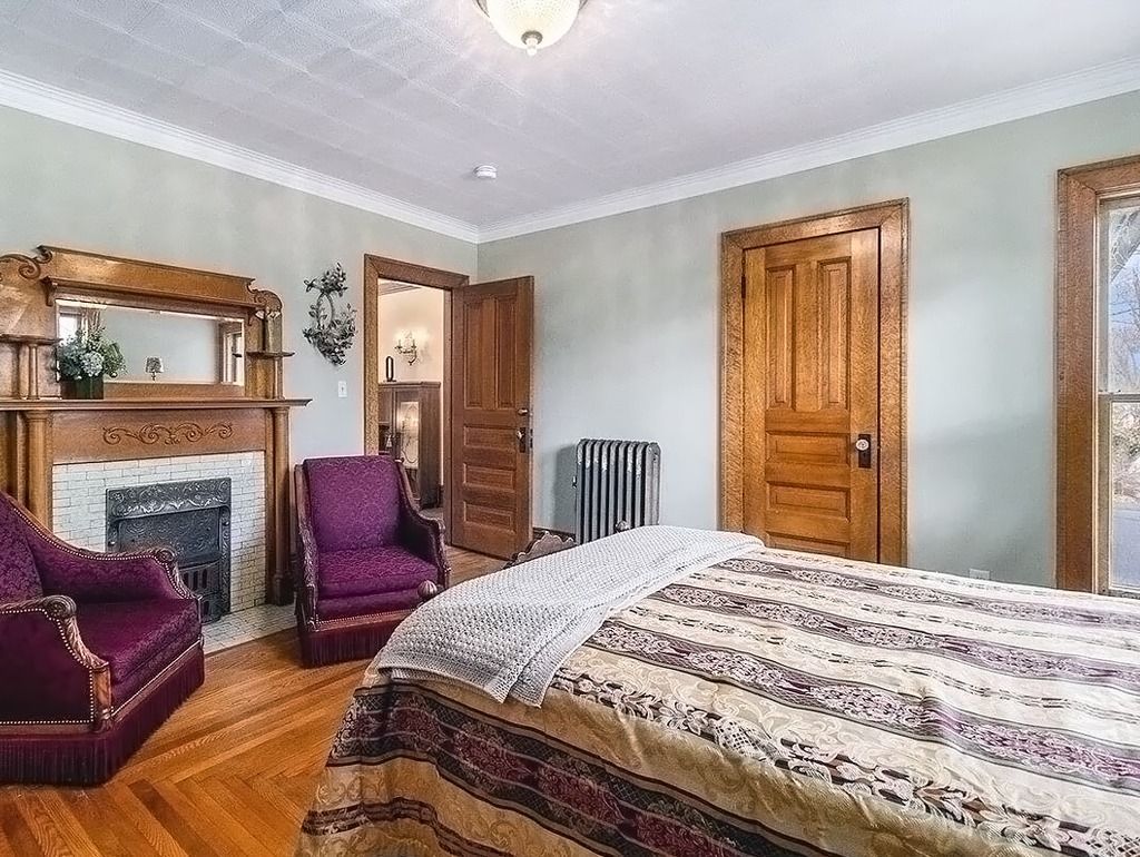 Bedroom with fireplace, wood floors, vintage furniture, light green walls, wooden door and trim.
