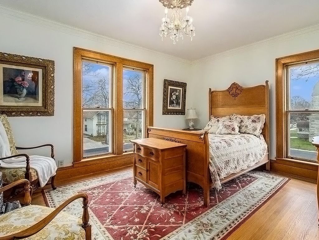 Bedroom with antique wooden furniture, red patterned rug, and two large windows.