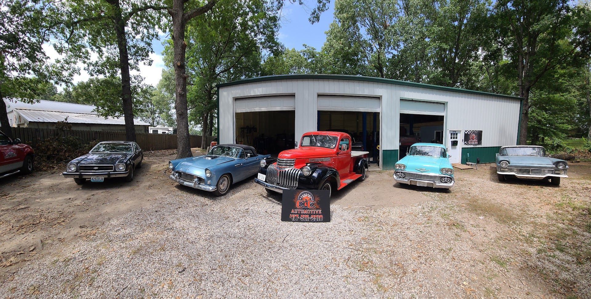 Classic cars parked outside a garage, including red, blue, turquoise, and gray cars on gravel. | C & C Automotive