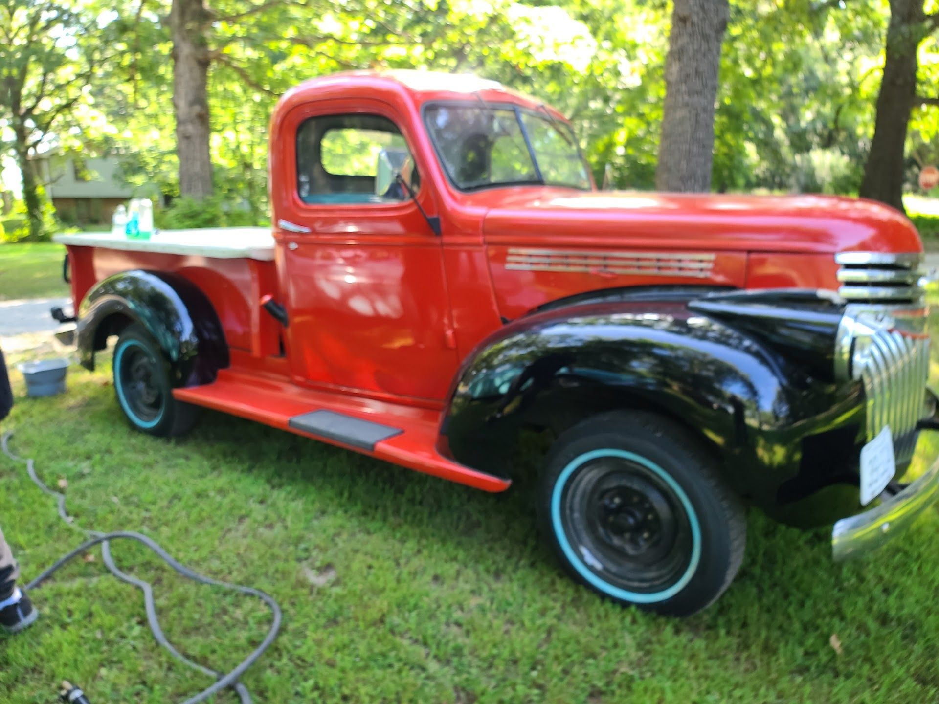 Red and black vintage pickup truck parked on grass in a sunny wooded area | C & C Automotive