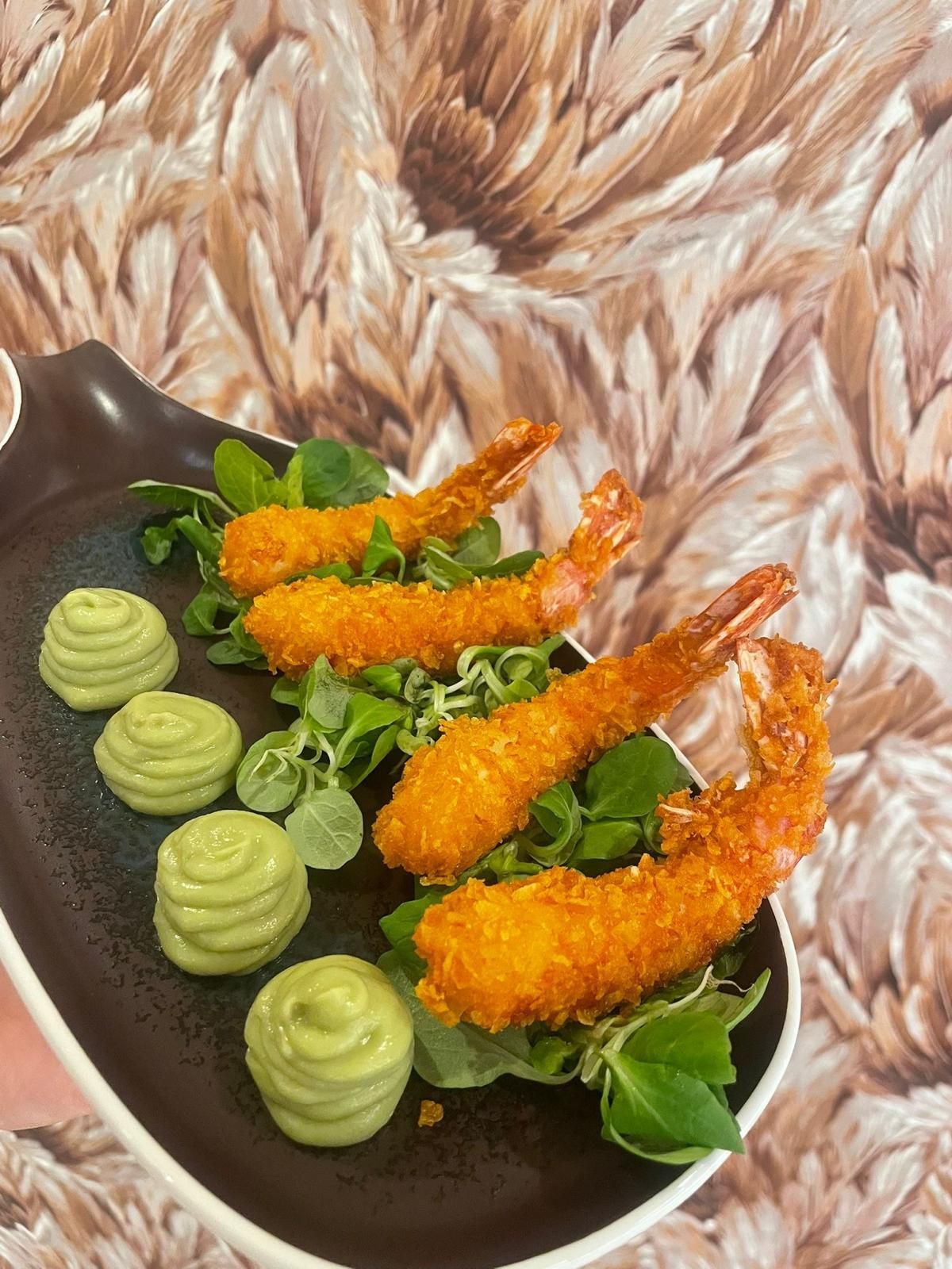 Gamberi in tempura con salsa verde su un piatto decorativo, su uno sfondo decorato.