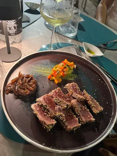 Tonno scottato con semi di sesamo, cipolle cotte e verdure, servito con vino bianco.