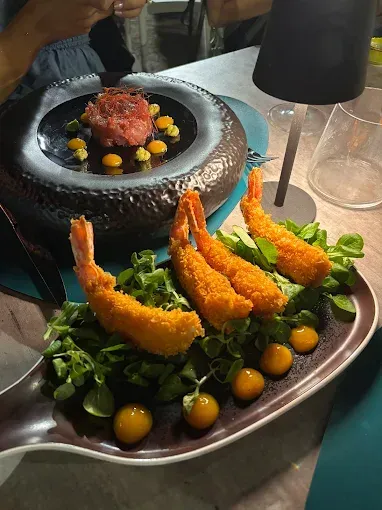 Piatto con gamberi impanati e tartare di manzo, guarnito con verdure e pois gialli.