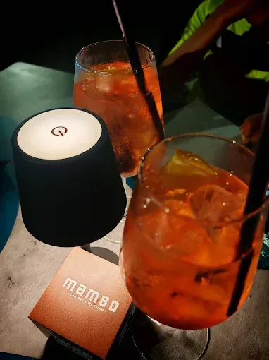 Due cocktail arancioni con ghiaccio e una lampada nera, accanto a un menù 