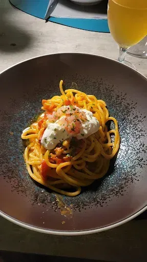 Piatto di spaghetti con salsa di pomodoro e una cucchiaiata di formaggio cremoso, in una ciotola scura, con un bicchiere di bevanda.