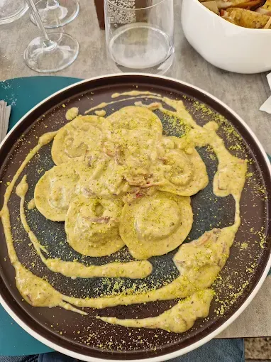 Piatto di ravioli in una cremosa salsa gialla, cosparsi di polvere verde.