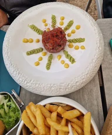 Tartare di manzo con salse decorative su piatto bianco; patatine fritte sotto.