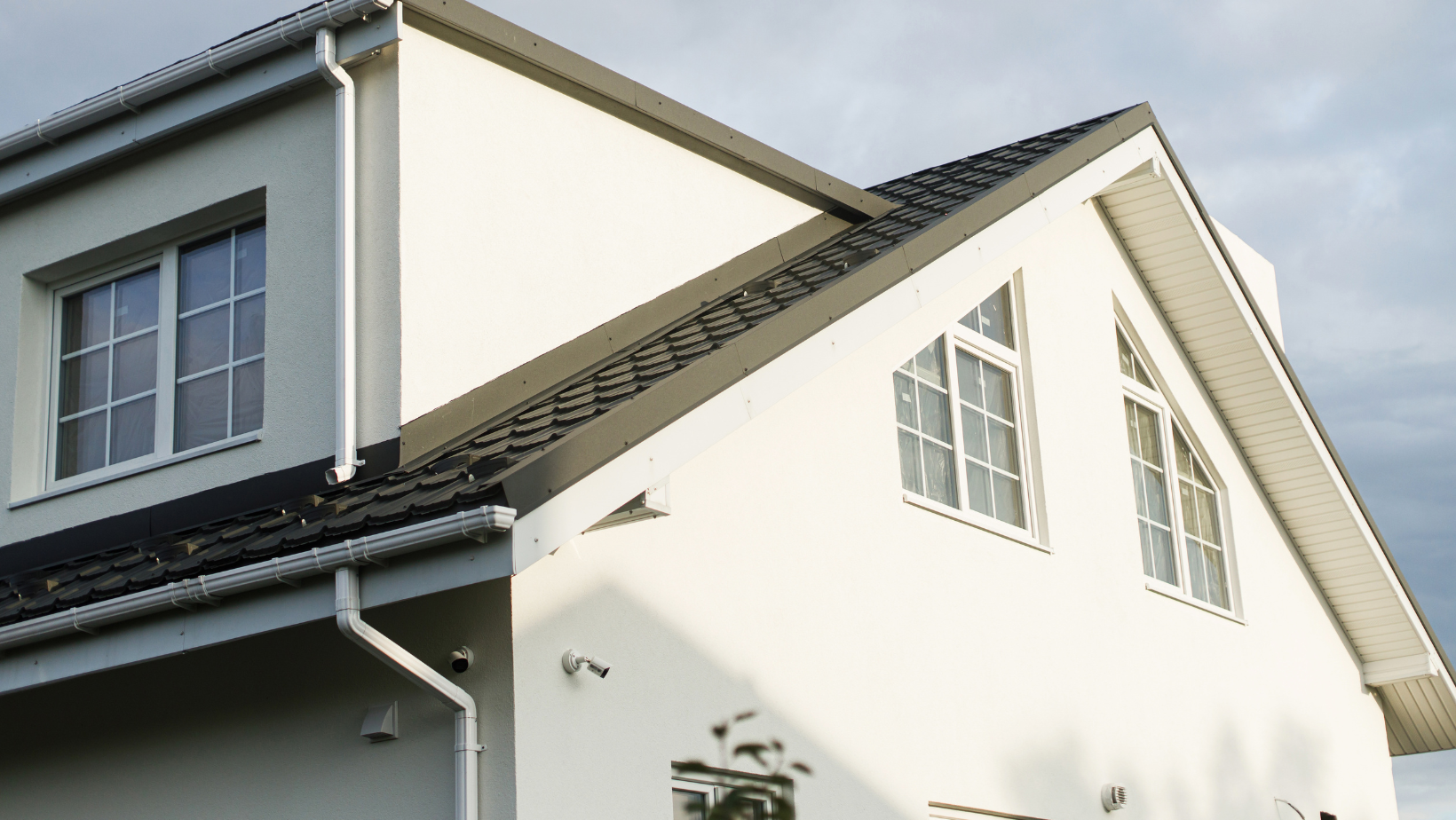 White house with dark roof and windows under a cloudy sky.