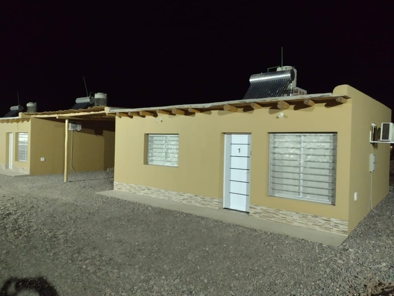 Dos edificios de una sola planta, de color canela, de noche. Cada uno tiene paneles solares en el techo, las puertas y las ventanas.