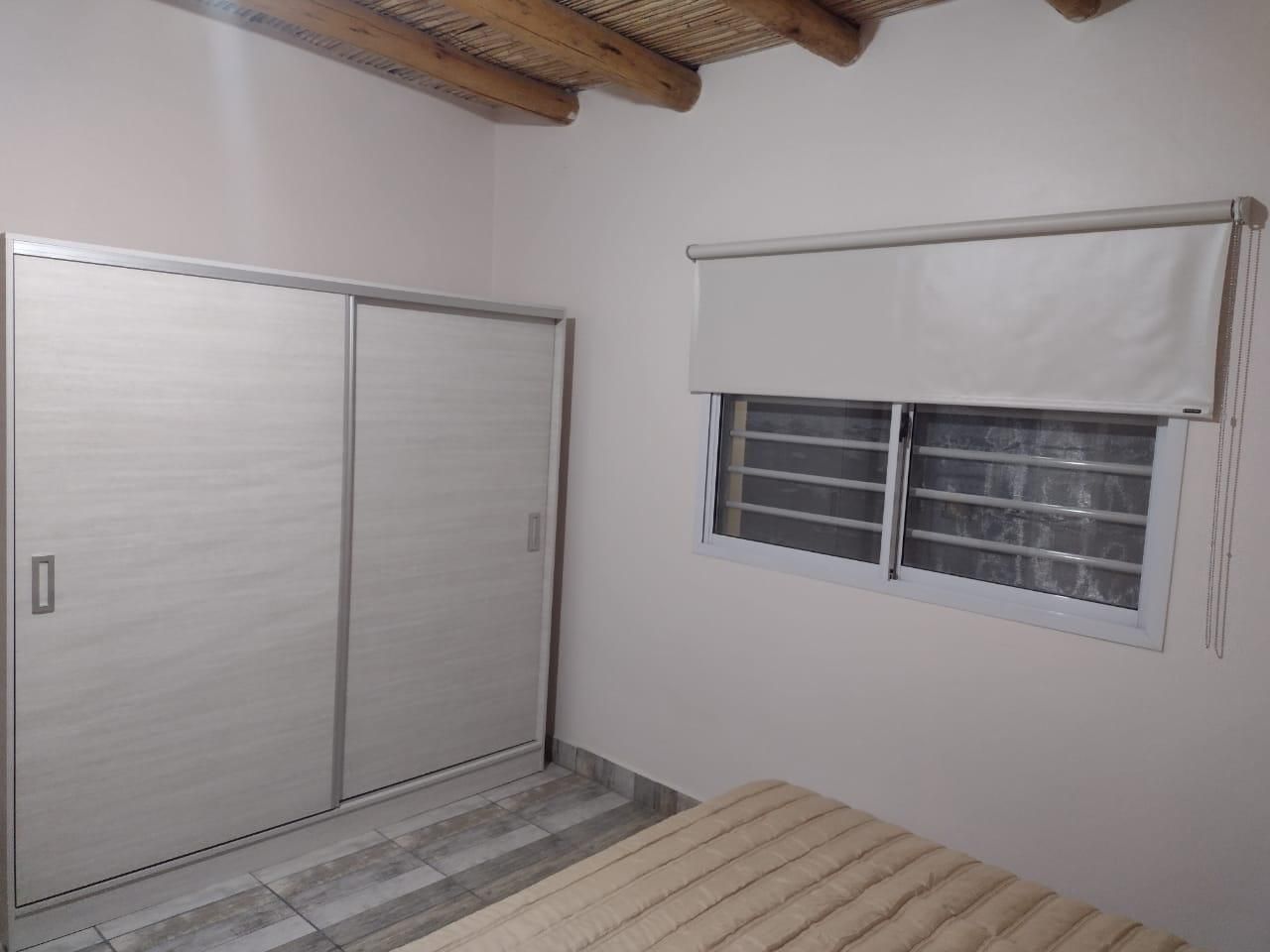Dormitorio con armario blanco, ventana con persiana y cama.