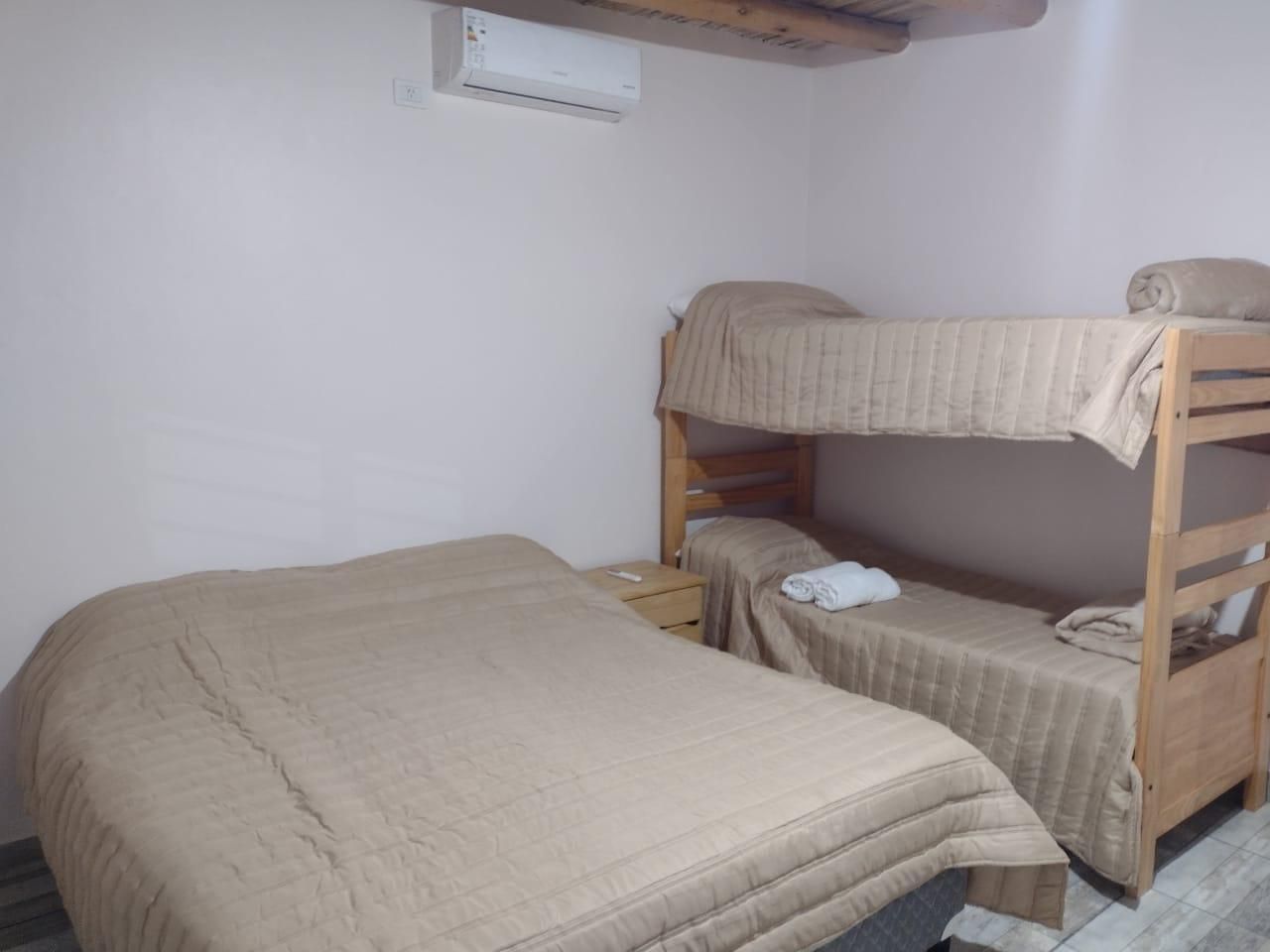 Dormitorio con cama doble, litera y aire acondicionado. Ropa de cama y paredes en beige.