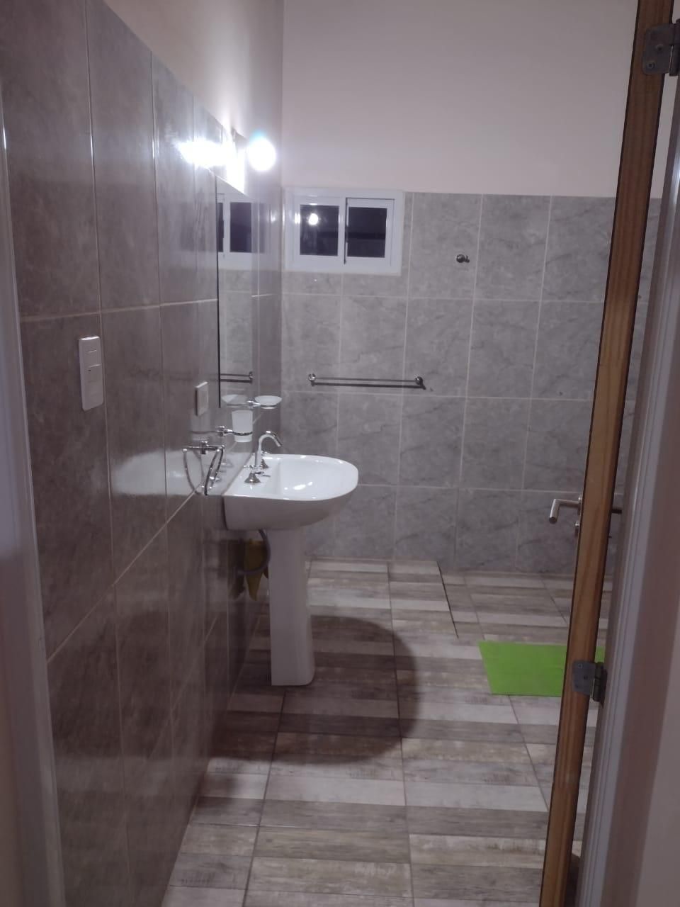 Pequeño baño con lavabo de pedestal, paredes revestidas de azulejos y puerta abierta.