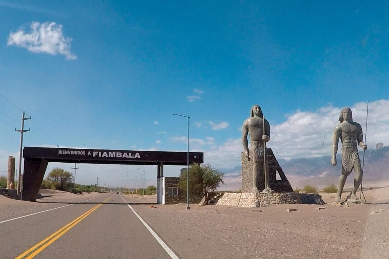 Entrada a Fiambalá, Argentina, marcada por un arco de piedra y estatuas de figuras indígenas bajo un cielo azul.