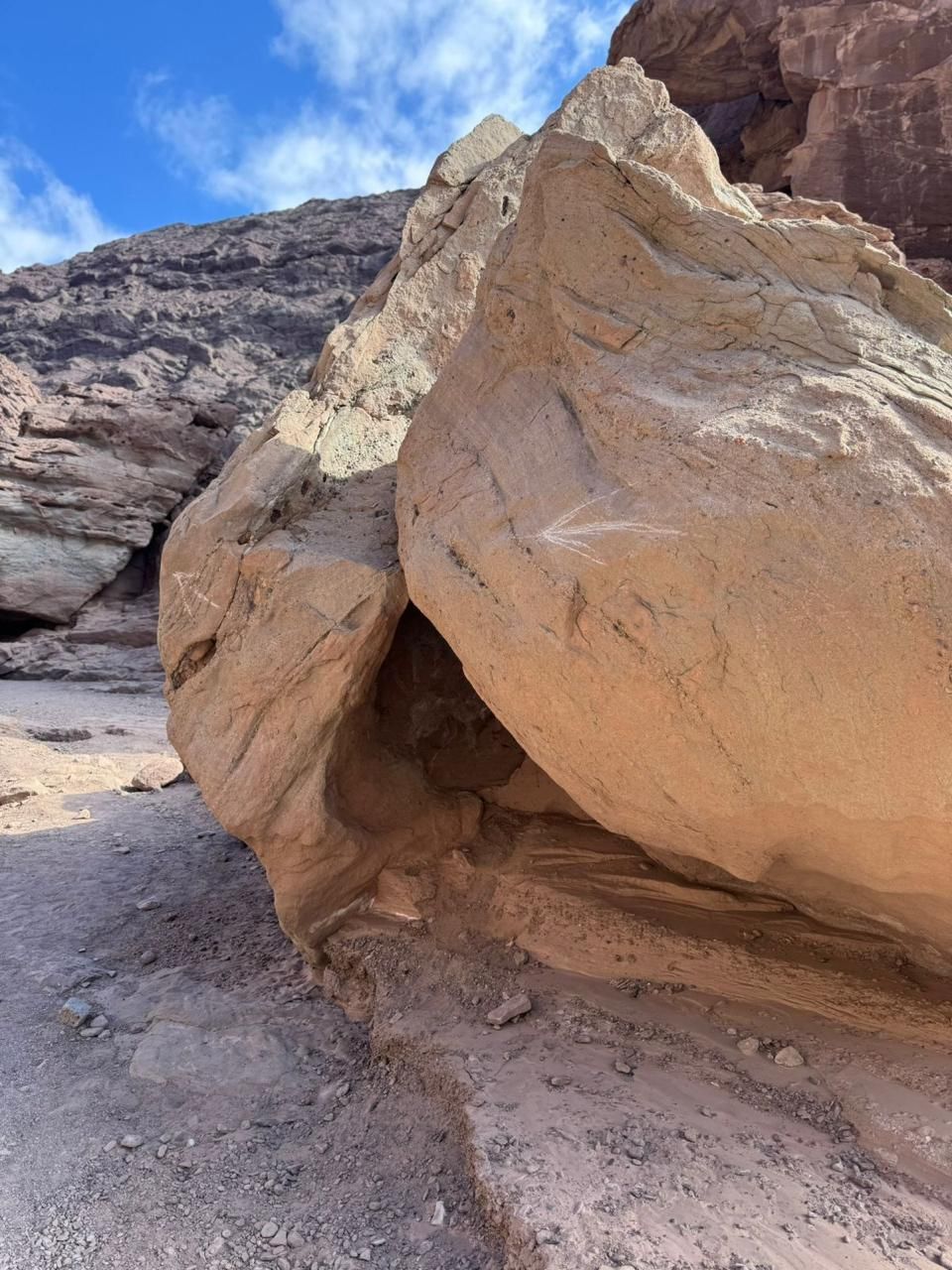 Gran formación rocosa de color canela en un paisaje desértico; cielo azul visible.