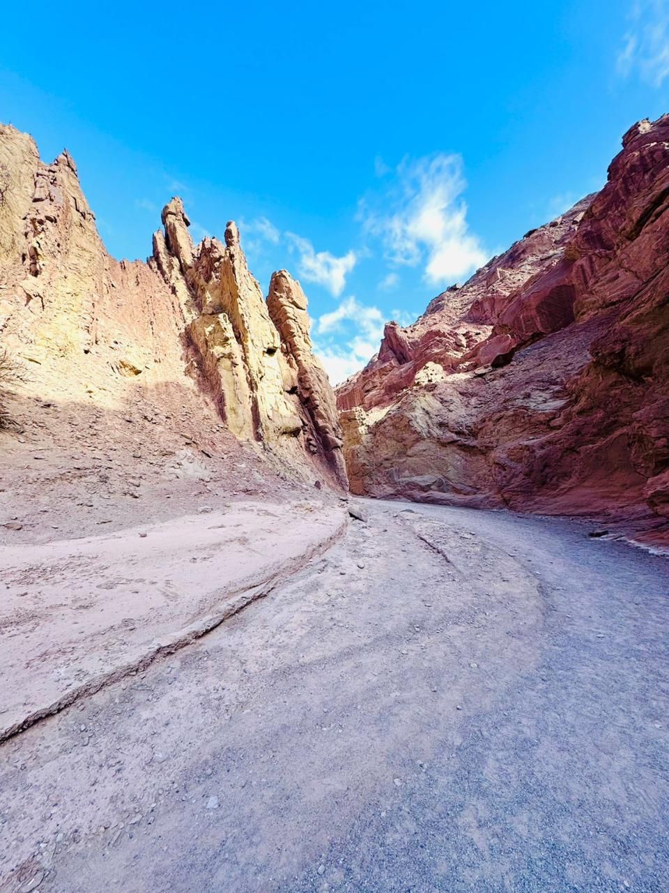 Cañón con paredes de roca de color rojo y tostado, suelo arenoso y cielo azul brillante.