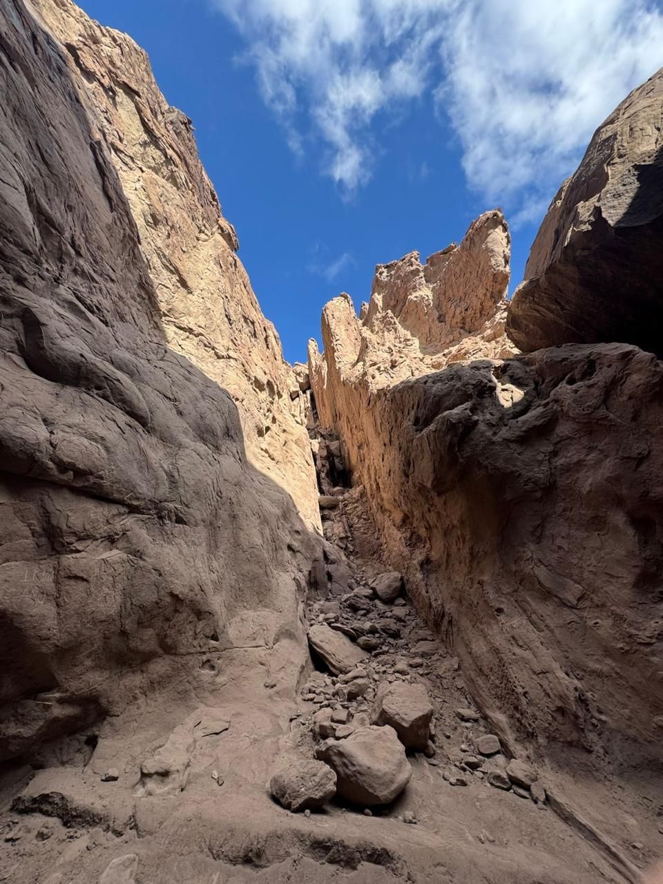 Cañón estrecho con paredes de roca de color marrón claro y cielo azul visible arriba.