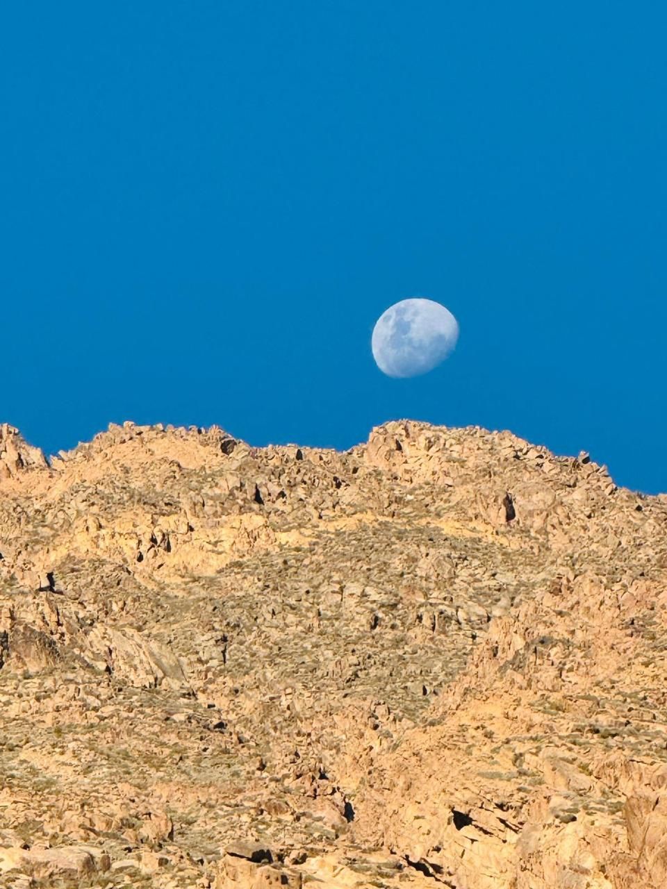 Cordillera bajo un cielo azul con luna creciente. Rocas marrones, cielo azul.