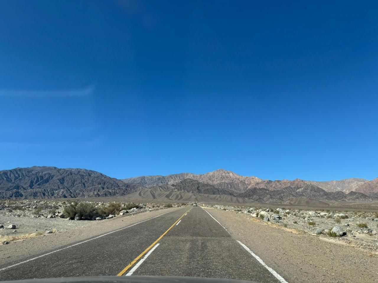 La carretera pavimentada se extiende hacia las montañas bajo un cielo azul brillante en un paisaje desértico.