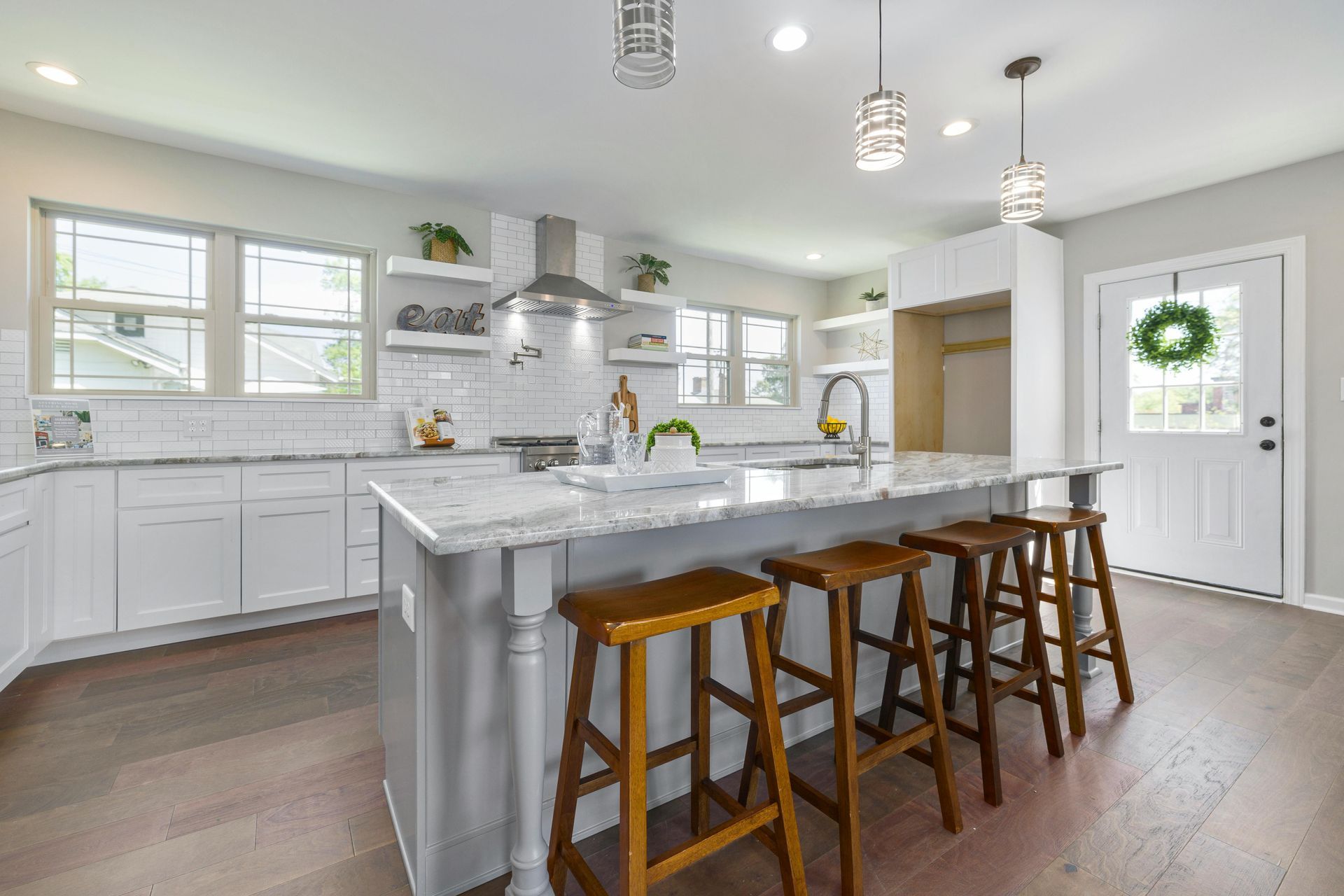 Modern kitchen with white cabinets, island with stools, wood floors, and a door with a wreath.