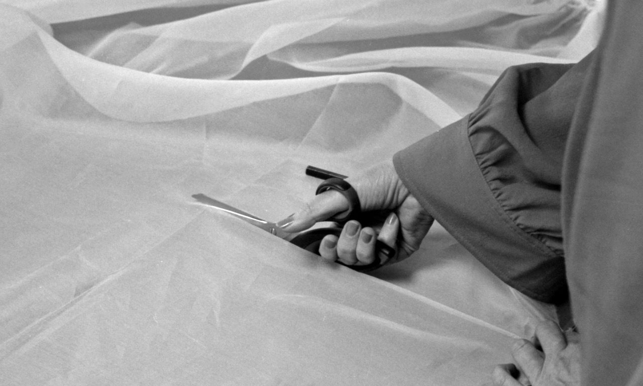 De hand van een coupeuse die met een schaar, voile knipt in een atelier.