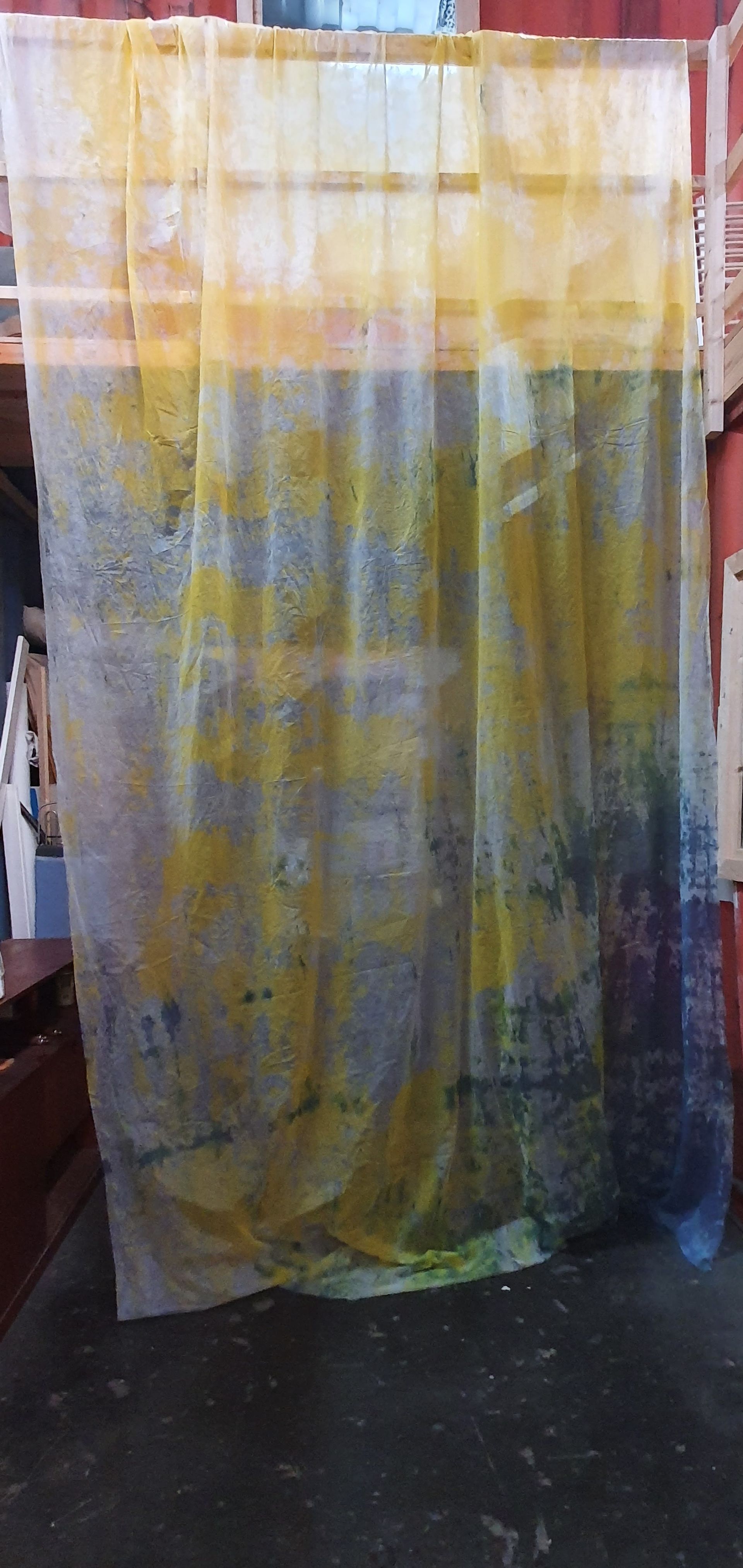 Abstract kunstwerk op een doorschijnend gordijn met gele, blauwe en groene verfspetters, hangend voor een donker oppervlak.