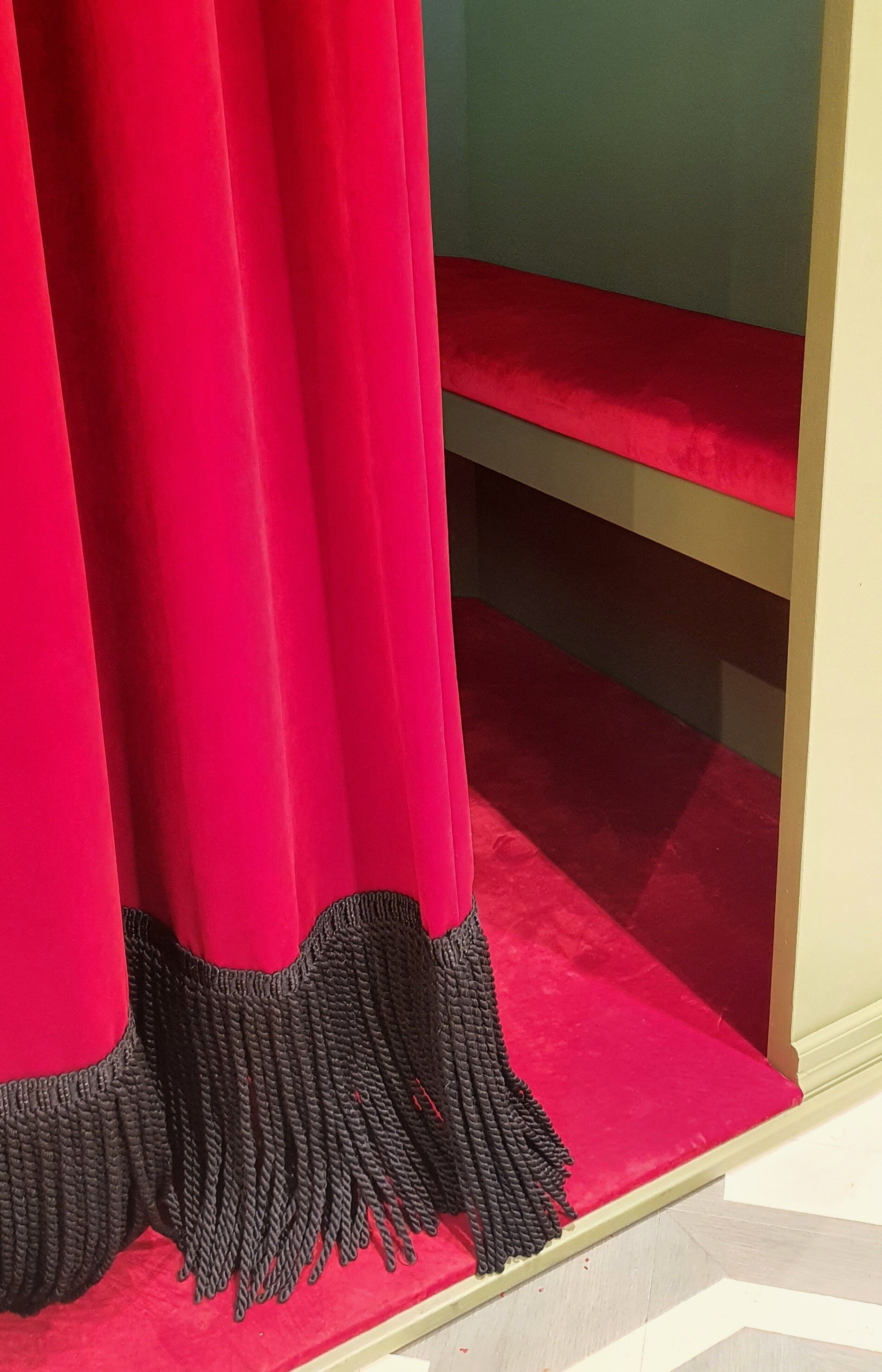 Rood fluweel gordijn met zwarte franjes, waardoor een met rood tapijt bedekte photobooth zichtbaar werd.