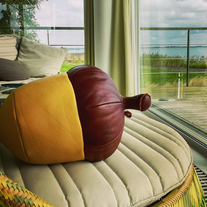 Eikelvormig kussen met geel en bruin leer, op een crèmekleurige stoel, met uitzicht op een meer.