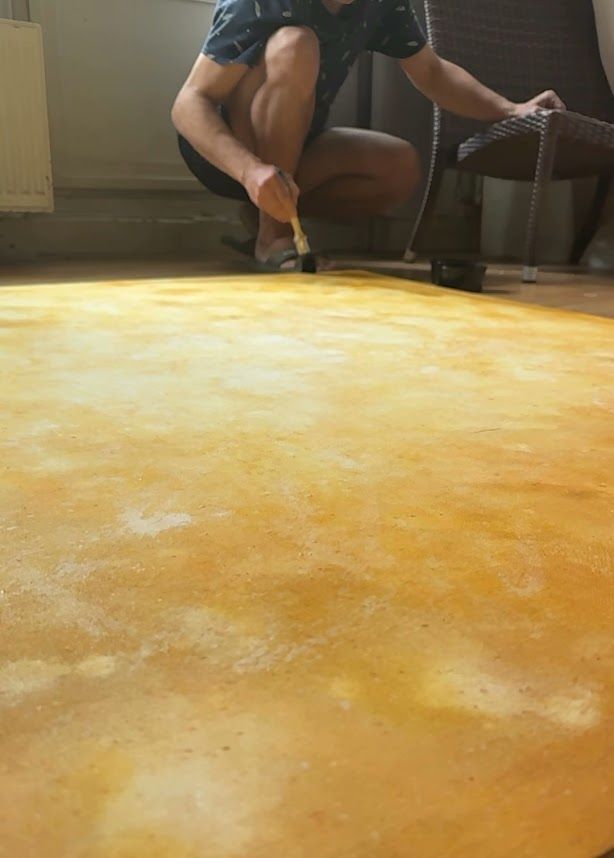 Man schildert een oranje-gele backdrop met een kwast, naast een fauteuil