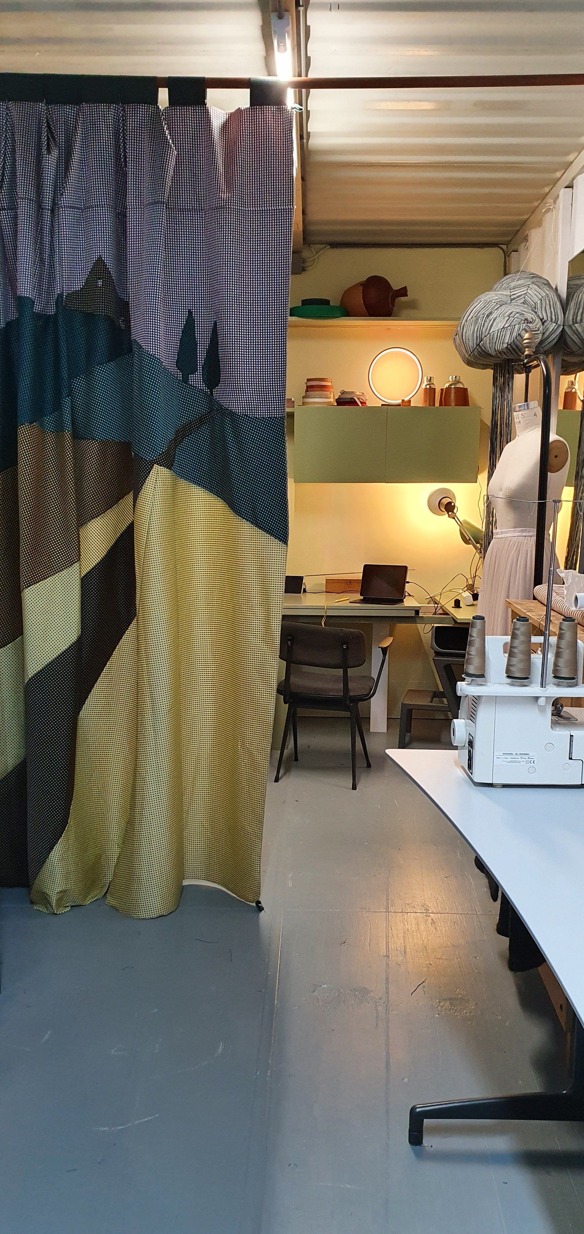 Interieur van een naaiatelier met stoffen gordijnen, naaimachine en een paspop.