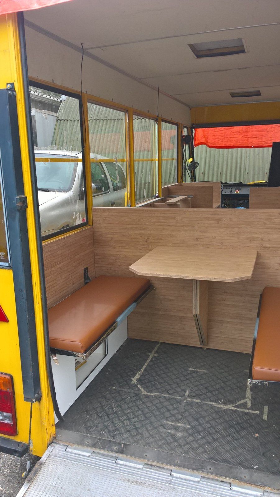 Interieur van een gele foodtruck met een tafel, banken en houten lambrisering.