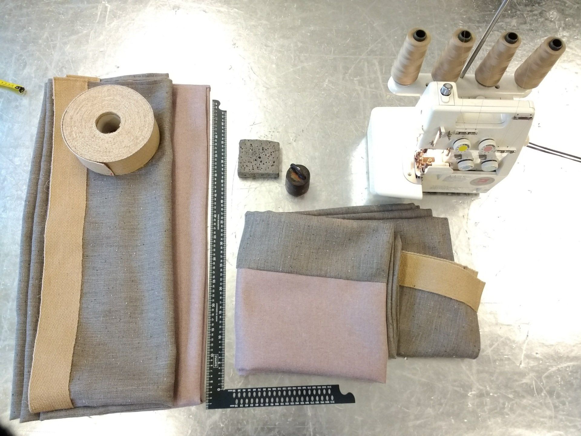 Uitgespreide naaimaterialen: stoffen, klosjes garen, een naaimachine en rollen kurk.