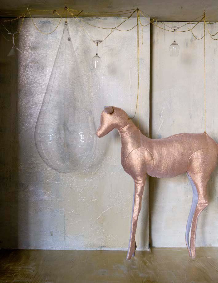 Een hangend hertenbeeld in een kamer met een grote, transparante, traanvormige bel. Lichtgouden accenten.