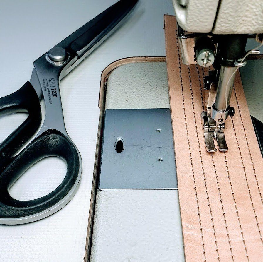 Naaimachine naait bruin leer met japanse  schaar in de buurt.