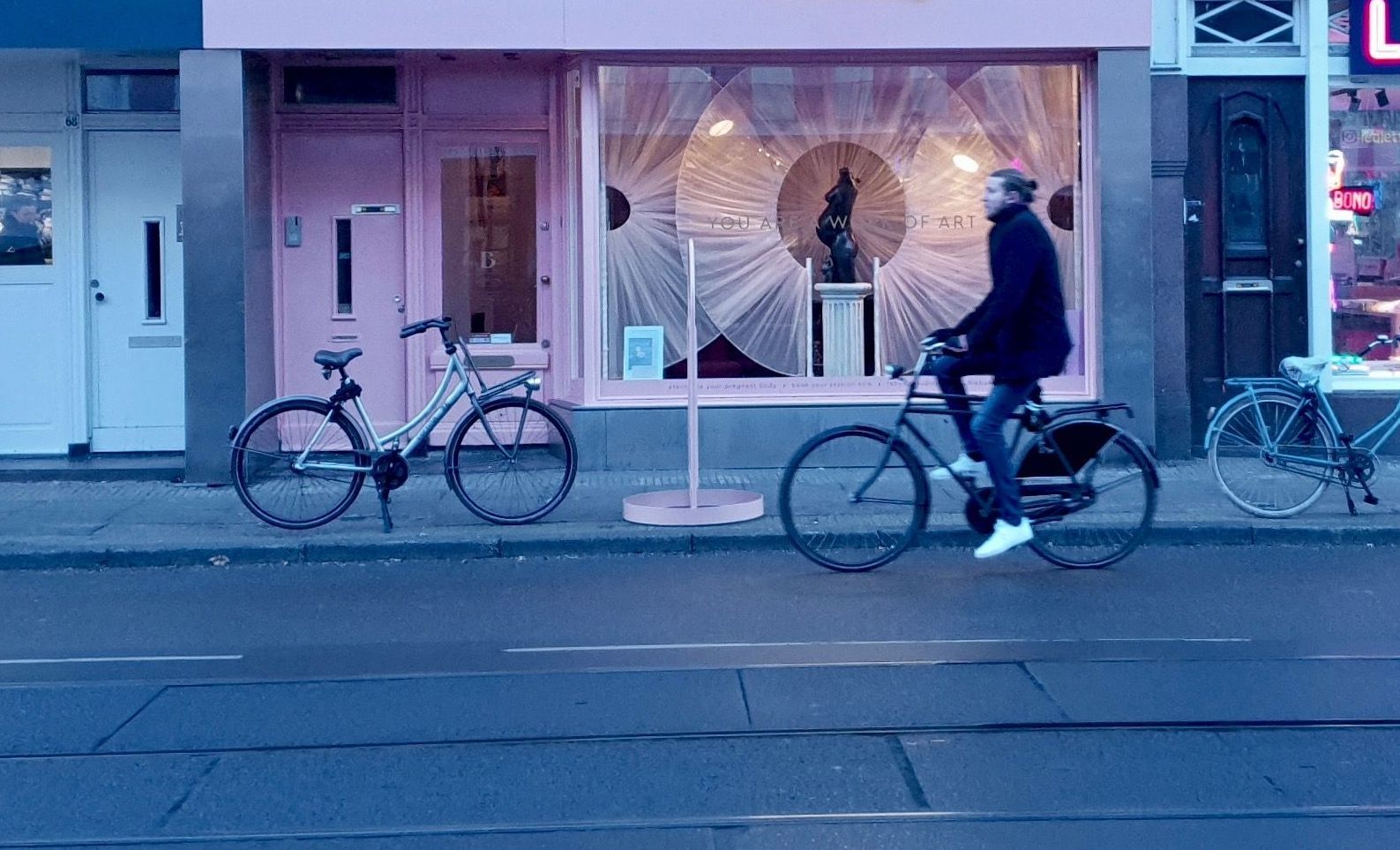 Man fietst langs een roze winkel, twee fietsen staan ​​ernaast geparkeerd. Stedelijke omgeving, blauwe tint.