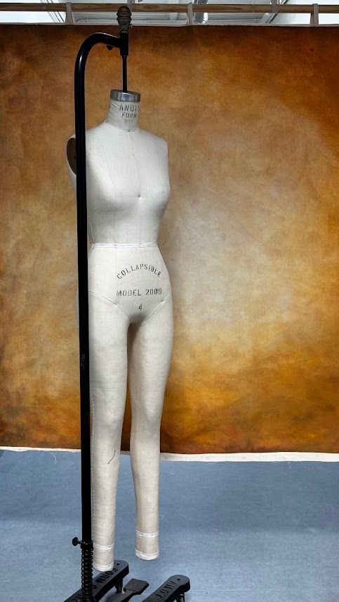 Mannequinvorm op standaard in studio-opstelling, bruine achtergrond, neutrale gele en bruine kleuren.