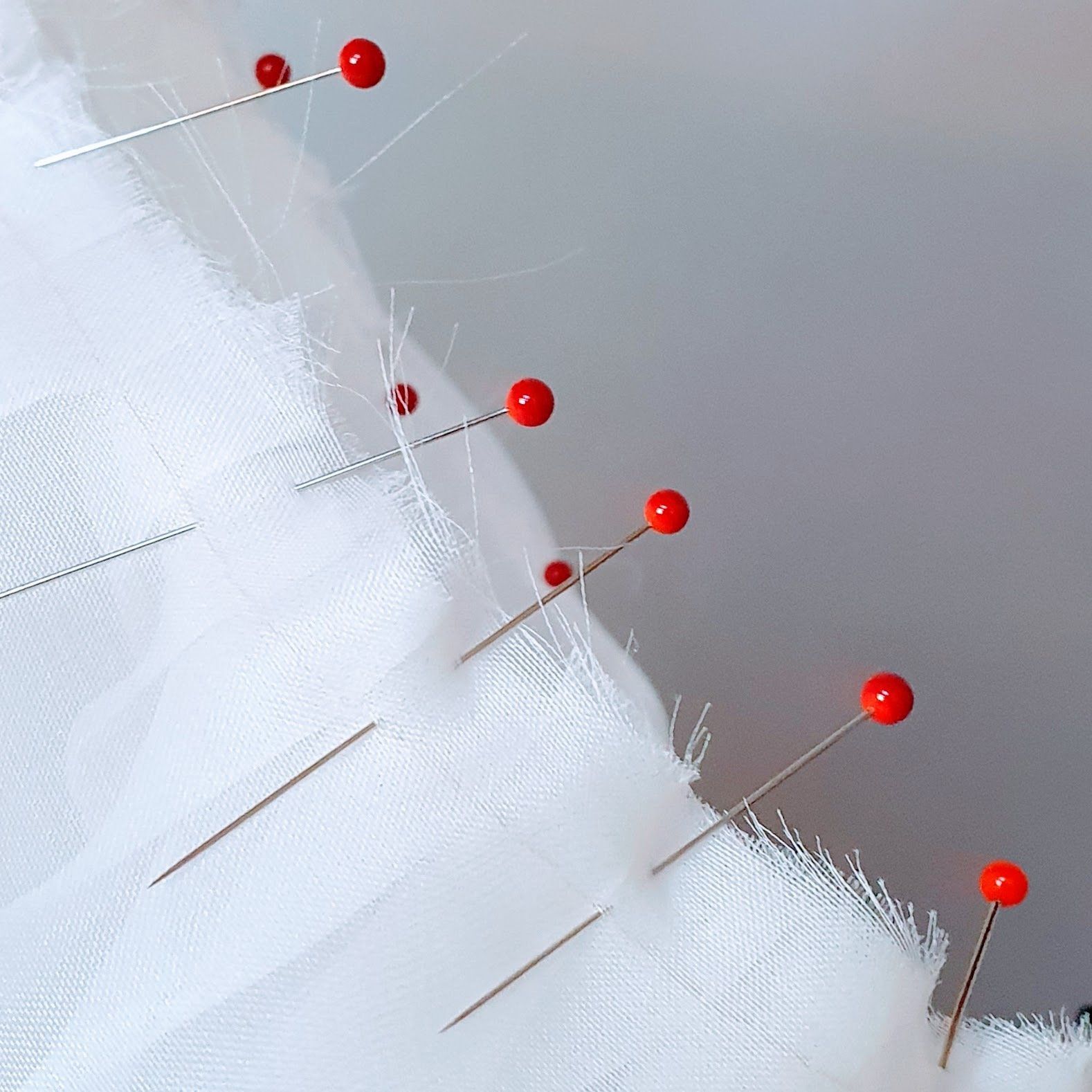 Red-headed pins secure white fabric against a gray surface.