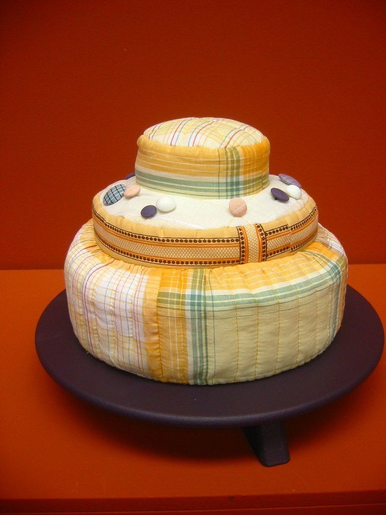  Taart, versierd met gele stof en pastelkleurige snoepjes, op een donkere taartstandaard tegen een oranje achtergrond.