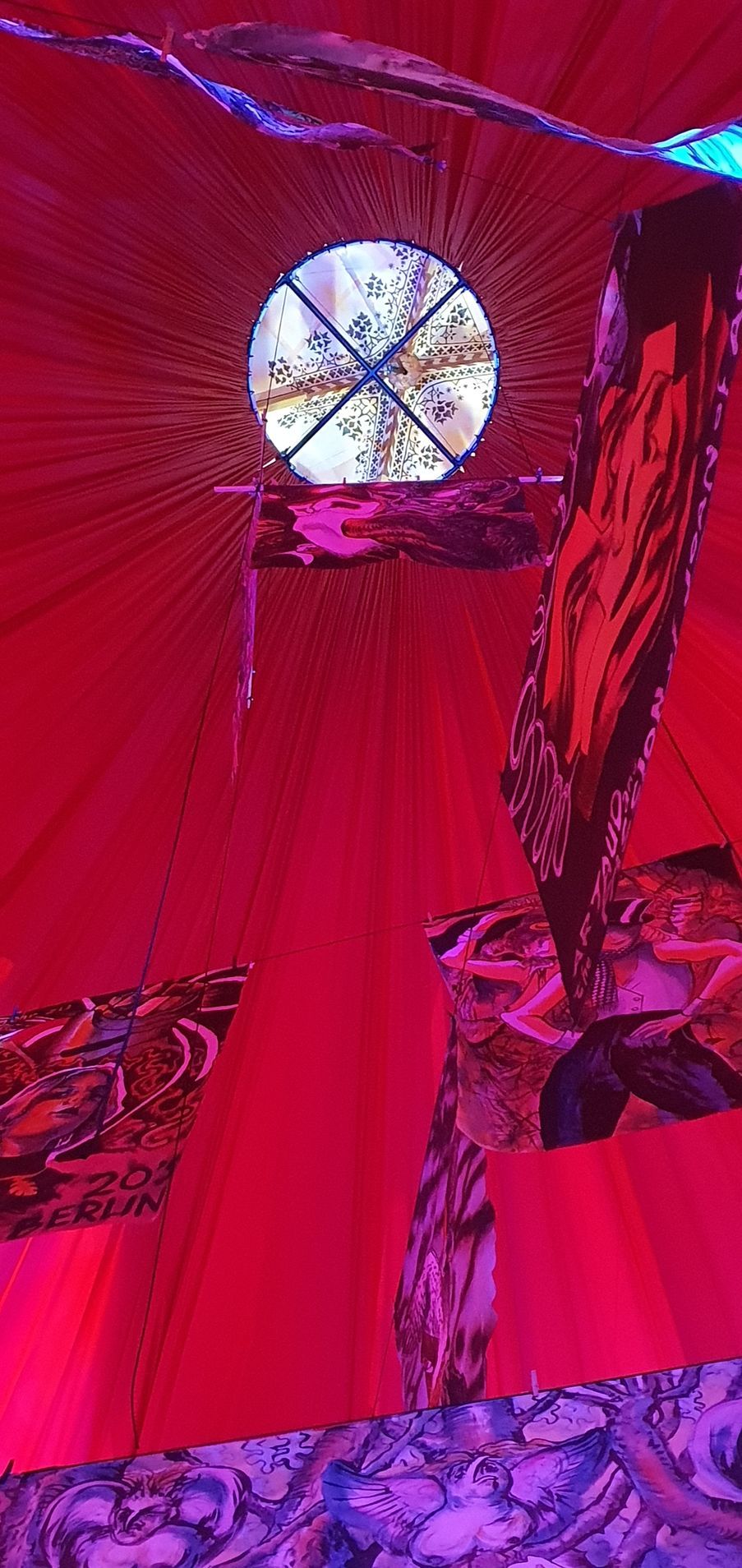 Felrode stof met een rond raam eroverheen, waar een zwart en rood designelement overheen hangt.