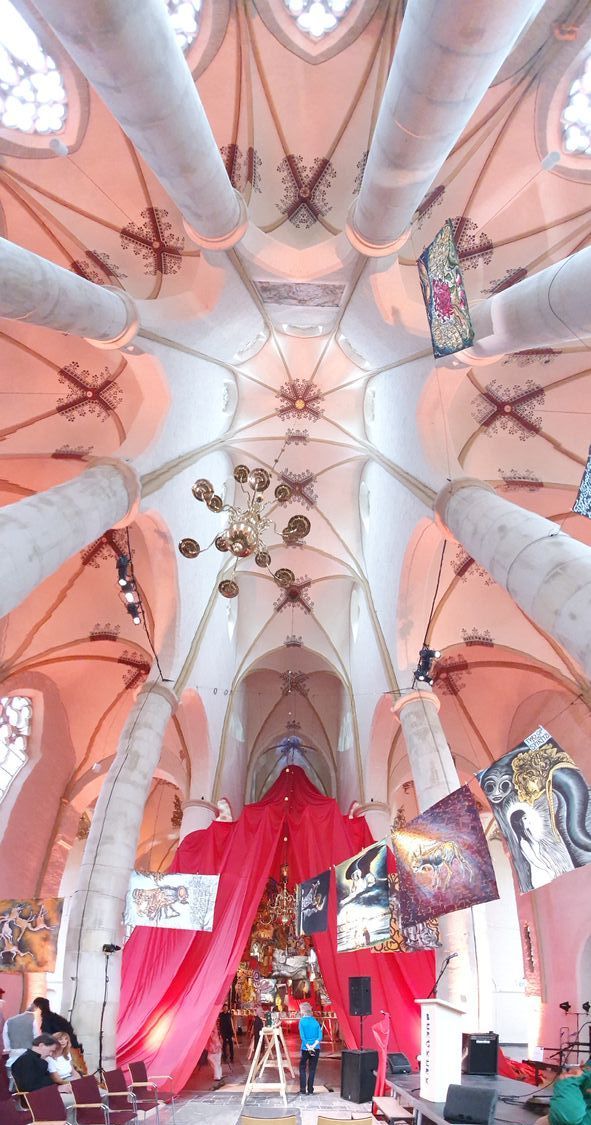 Uitzicht van bovenaf op een kathedraal met hoge witte zuilen, een rijkversierd plafond, rode decoraties en wat mensen.