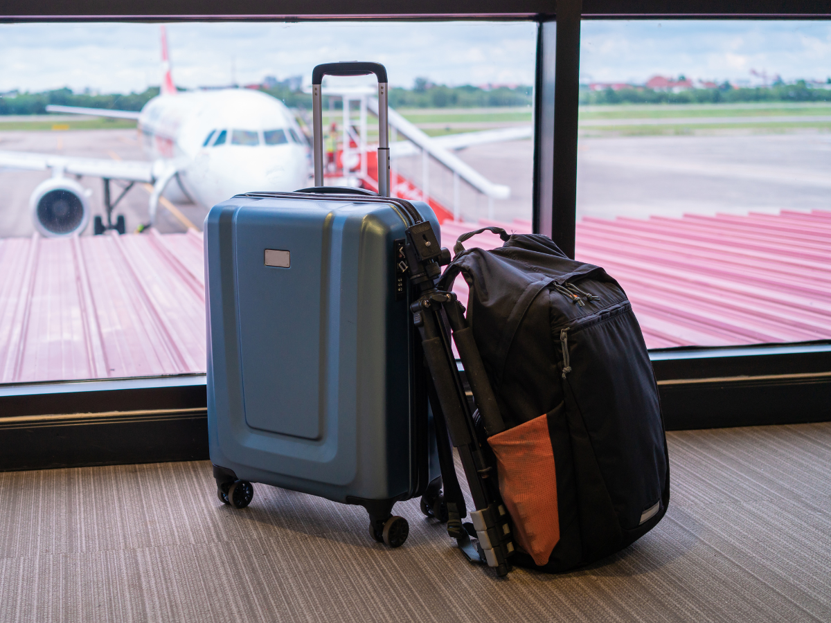 Blue suitcase and black backpack at an airport window, plane in the background.